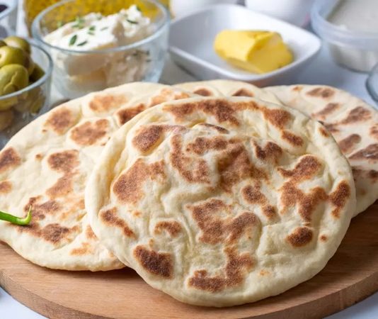 Bazlama, Türk mutfağının en eski ve en bilinen ekmeklerinden biridir. Tarihi, Osmanlı dönemi ve öncesine kadar uzanır. Özellikle köylerde ve taş fırınlarda yapılan bazlama, sabah kahvaltılarının ve yemeklerin vazgeçilmez bir parçası olmuştur. Hamurun mayalanması ve sac üzerinde pişirilmesi, ona kendine özgü yumuşak ve hafif kabarık dokusunu kazandırır. Konulu bir haber görseli.