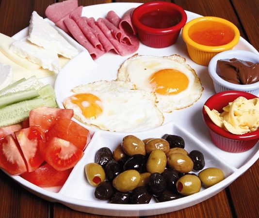 Türk mutfağında kahvaltı yalnızca güne başlamak için yapılan bir öğün değil, aynı zamanda kültürel bir gelenektir. Tarih boyunca ailelerin bir araya geldiği, dostların sohbet eşliğinde vakit geçirdiği sofraların baş tacı olmuştur. Özellikle pazar günleri kurulan geniş kahvaltı sofraları, hem çeşitliliğiyle hem de paylaşımın verdiği mutlulukla öne çıkar. Konulu bir haber görseli.