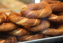 Simit, Osmanlı döneminden günümüze kadar gelen köklü bir geçmişe sahiptir. İlk olarak saray mutfaklarında farklı un karışımlarıyla yapılan bu lezzet, zamanla halk arasında yaygınlaşarak günlük yaşamın bir parçası haline gelmiştir. Özellikle 16. yüzyıldan itibaren İstanbul’da simit fırınlarının açılmasıyla birlikte, bu eşsiz yiyecek şehir kültürünün önemli bir unsuru olmuştur. Bugün Anadolu’nun dört bir yanında farklı isimlerle anılsa da, ortak nokta simidin sofralarda her daim yer bulmasıdır. Konulu bir haber görseli.