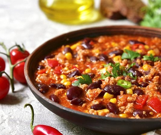 Chili Con Carne, Meksika ve Amerika mutfaklarının kesişim noktasında doğmuş, dünya genelinde tanınan baharatlı bir yemektir. İsminin anlamı “etli biber” olup, temelinde kırmızı biber ve dana eti yer alır. Kökeni konusunda farklı tartışmalar bulunsa da genellikle Meksika kökenli olduğu kabul edilir. Ancak Texas mutfağının da bu yemeğin yaygınlaşmasında büyük payı vardır. Konulu bir haber görseli.