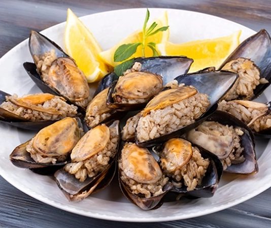 Midye Dolma: Sokakların Vazgeçilmez Lezzeti Türk mutfağının en bilinen sokak lezzetlerinden biri olan midye dolma, kökeni Osmanlı dönemine kadar uzanan köklü bir geçmişe sahiptir. Saray mutfağında farklı baharatlarla hazırlanan pirinçli yemeklerin deniz ürünleriyle birleşmesi sonucu ortaya çıktığı düşünülmektedir. Zamanla bu lezzet, sokaklara taşınarak herkesin ulaşabileceği bir hale gelmiştir. Konulu bir haber görseli.