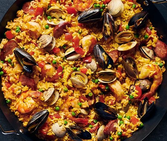 Paella, İspanya’nın en bilinen yemeklerinden biri olarak dünya mutfağında önemli bir yere sahiptir. Özellikle Valencia bölgesinde ortaya çıkan bu yemek, zamanla tüm ülkeye ve oradan da dünyaya yayılmıştır. Tarihi 15. yüzyıla kadar uzanan paella, köylülerin tarlalarda buldukları malzemeleri bir araya getirerek pişirdikleri pratik bir yemek olarak doğmuştur. Konulu bir haber görseli.