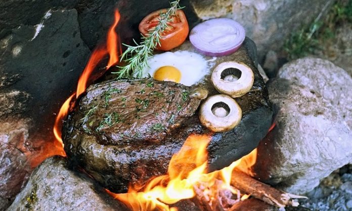 Yemek pişirme teknikleri, insanlık tarihinin en eski kültürel pratiklerinden biri olarak kabul edilir. Bu teknikler arasında yer alan Isıtılmış Taş Üzerinde Pişirme, doğayla doğrudan temas kuran, ilkel ama bir o kadar da etkili bir yöntem olarak öne çıkar. Ateşle ısıtılan taşların üzerinde ya da taşların yardımıyla yapılan bu pişirme biçimi, hem tarihsel hem de kültürel açıdan güçlü anlamlar taşır. Günümüzde gastronomi dünyasında yeniden ilgi gören bu yöntem, geçmişle bugünü aynı sofrada buluşturur. Konulu bir haber görseli.