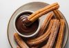 Churros, son yıllarda yalnızca İspanya’nın geleneksel sokak lezzeti olmaktan çıkıp dünya genelinde kafe menülerinin favorisi haline geldi. Özellikle Türkiye’de tatlı kültürünün giderek çeşitlenmesiyle birlikte churros popüler bir alternatif olarak öne çıkıyor. Çıtır yapısı, şeker ve tarçınla kaplanan dış yüzeyi ve sıcak çikolata sosuyla birleştiğinde ortaya çıkan benzersiz tat, birçok insanın yeni gözdesi haline gelmiş durumda. Konulu bir haber görseli.