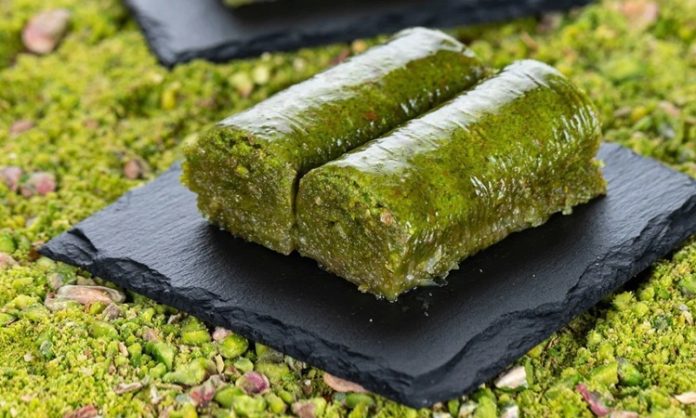 Fıstıklı sarma, Türk tatlı kültürünün hem tarihsel hem damak zevki açısından en özel lezzetlerinden biri olarak biliniyor. Osmanlı saray mutfağından günümüze taşınan zengin mirasın bir parçası olan bu tatlı, özellikle özel günlerde, bayram sofralarında ve davet masalarında sıklıkla tercih ediliyor. Bu nedenle sadece gastronomik bir tatlı olmakla kalmayan fıstıklı sarma, kültürel bir simge haline gelmiş durumda. Şerbetli tatlılar arasında kendine özgü yapısıyla farklı bir yer edinen bu lezzet, hem yapımı hem sunumu hem de ustalığıyla dikkat çekiyor. Konulu bir haber görseli.